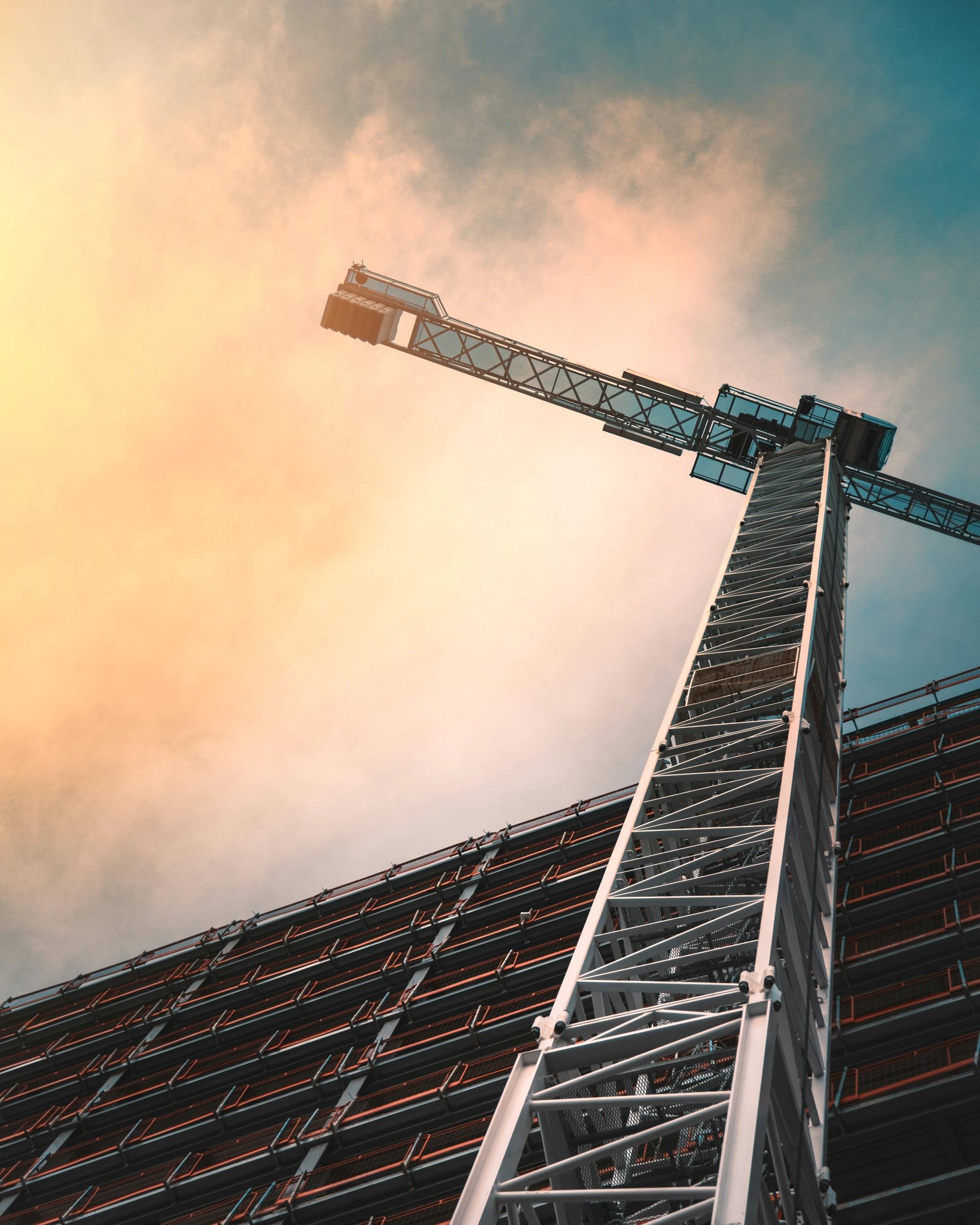 A tower crane against a golden sky, seen from a building under construction